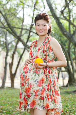Beautiful asian pregnant woman portrait in public park hold one orange fruit in hand - photo taken 2 days before baby birthの写真素材