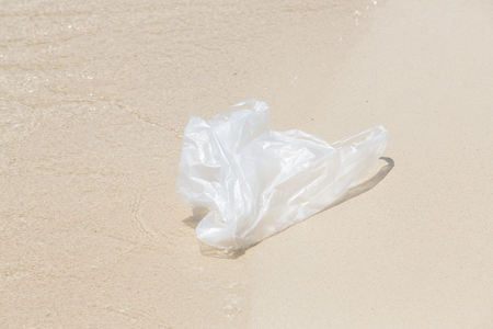 Close up plastic bag on sand and sea water, waste on beachの写真素材
