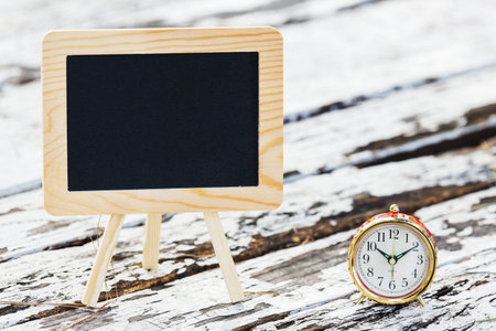 Blank small blackboard with alarm clock on grunge wooden table