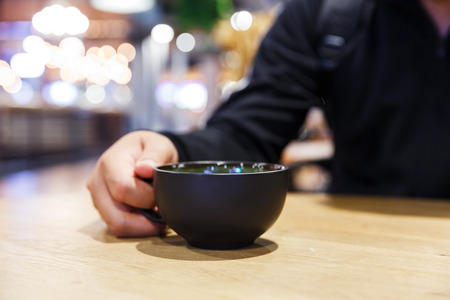 Close up black color coffee cup or mug on hand on wooden table with blur background, business concept, refreshment breakの写真素材