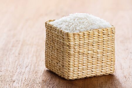 Close up Thai jasmine rice in wicker basket on wooden tableの写真素材