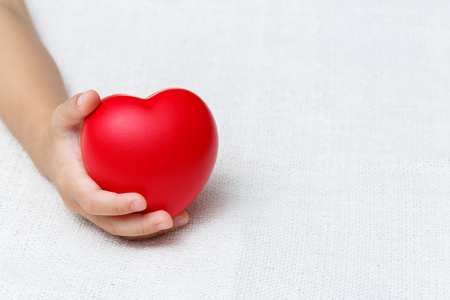 Baby hold red color heart in palm hands, love and health conceptの写真素材