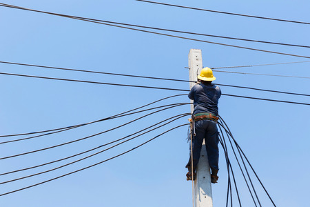 Electrician with yellow color safety helmet wiring electric cable on pole, energy conceptの写真素材