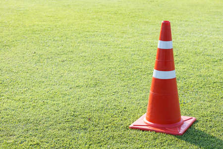 red plastic traffic cone on green grass field lawn with silver color reflective stripの写真素材