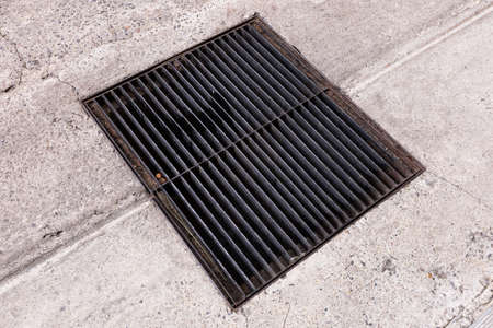 Closeup grunge old and rusty steel drainage grating on concrete road, street sewage cover in cityの写真素材