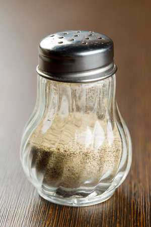 Close up ground white pepper in glass bottle on wooden table, hot seasoning spice powdered ingredient for cookingの写真素材