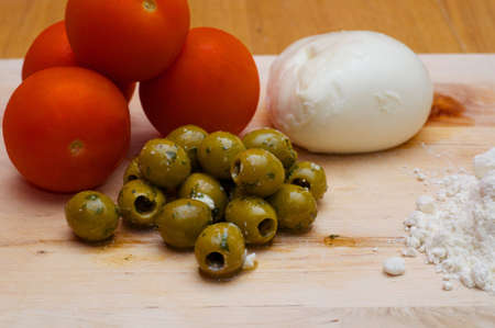 Tomatoes, Flour, Mozzerella and Olives in a pile on a chopping boardの写真素材