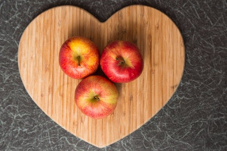 Three red and yellow apples on Heart Shaped Chopping Boardの写真素材