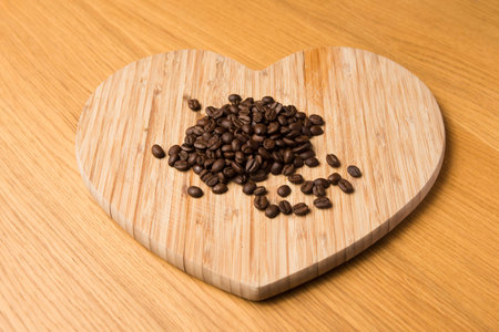Dark Coffee Beans on Heart Shaped Chopping Board on a wooden tableの写真素材