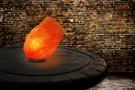 Himalayan salt as a lamp on an old wooden table in front of a brickwallの写真素材