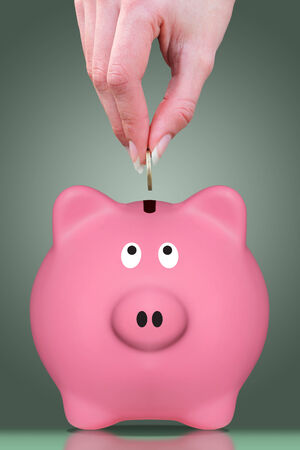 Female hand putting a coin in a piggy bankの写真素材