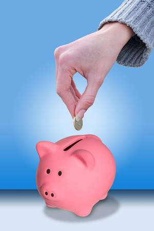 Female hand putting a coin euro in a piggy bankの写真素材