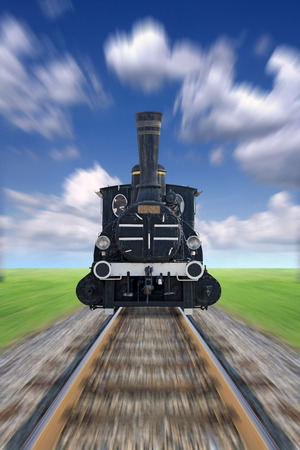 An old steam powered locomotive, railway track, green grass and blue sky blurredの写真素材