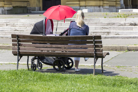 Mothers and baby in stroller, sitting on benchの写真素材