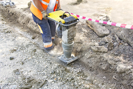 Worker uses compactor to firm soil at worksiteの写真素材