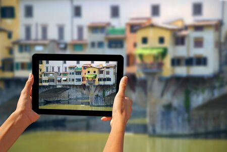 Girl taking pictures on a tablet Ponte Vecchio is a famous medieval bridge over the River Arno in Florence, Italyの写真素材