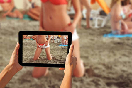 Girl taking pictures on a tablet Young beautiful girls on a sandy beachの写真素材