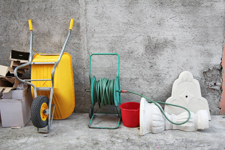 Wheelbarrow, hose and cartons in front of the concrete wall の写真素材