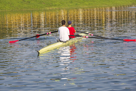 Two rowers in a boat, paddles on the tranquil lakeの写真素材