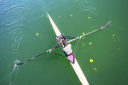 The woman rower in a boat, rowing on the tranquil lakeの写真素材