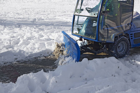 Blue snowplow removing snow from sidewalk and sprinkled salt antifreezeの写真素材