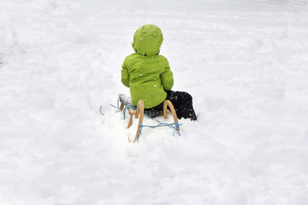 Child in a green jacket enjoying a sleigh ride in a snowy winter parkの写真素材