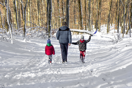 Rear view on two children with Dad while walking in the snow forestの写真素材