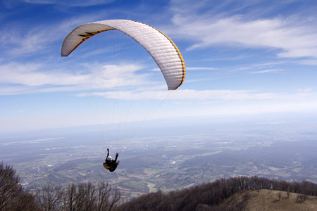 Paraglider flying over mountains to the valleyの写真素材