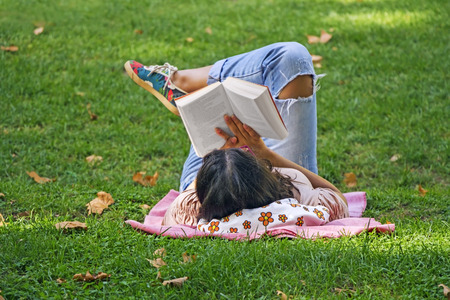 Young girl reading a book lying in the grass in the parkの写真素材