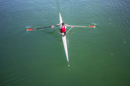 Young man Rower in a boat, rowing on the tranquil lakeの写真素材