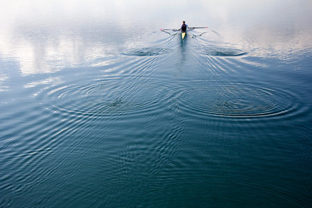 Young man in a boat, rowing on the tranquil lakeの写真素材