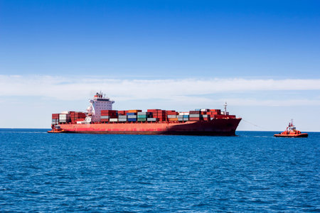 Tugboats pulling container cargo ship to harbor