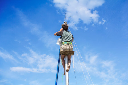 Young man hanging and repairs yacht mast