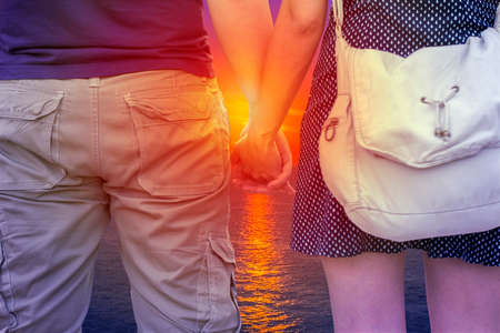 Young couple holding hands on beach at sunsetの写真素材