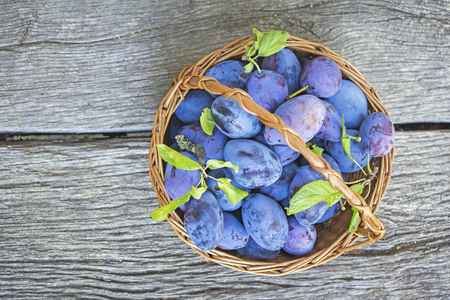 Plums in a wicker basket on the wooden backgroundの写真素材