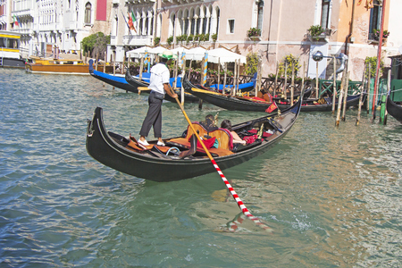 Venetian gondolier in the gondola is transported tourists through canal waters of Venice Italyの写真素材