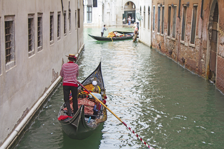 Venetian gondolier in the gondola is transported tourists through canal waters of Venice Italyの写真素材