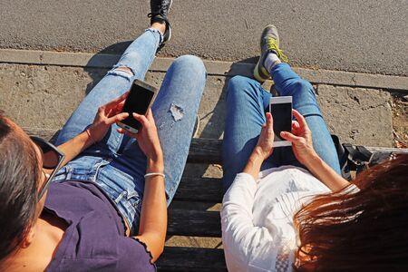 Two young girls watching smart mobile phonesの写真素材