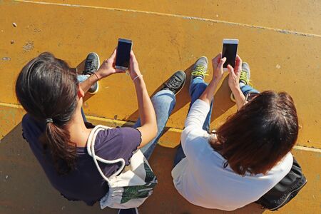 Two young girls watching smart mobile phonesの写真素材