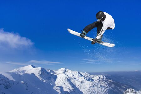 Skier Snowboarder jumping through air with blue sky in backgroundの写真素材