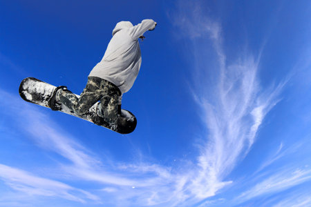 Skier Snowboarder jumping through air with blue sky in background