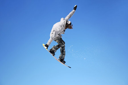 Snowboarder jumping through air with blue sky in background