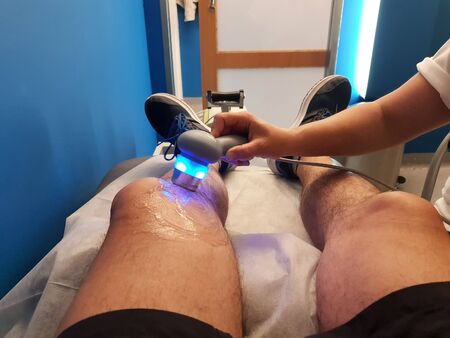 Physiotherapist is applying ultrasound therapy on the knee injury with ultrasound head transducerの写真素材