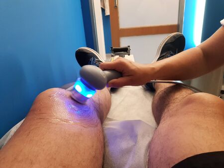 Physiotherapist is applying ultrasound therapy on the knee injury with ultrasound head transducer, blured motionの写真素材