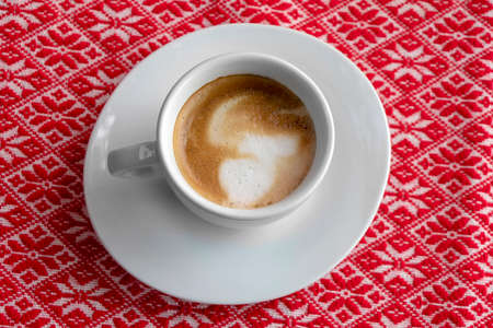White cup of coffee with foam and bubbles on a red tableclothの写真素材