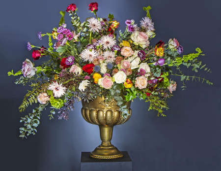 A Beautiful large flower bouquet with a lot of different flowers in a golden pot, on a blue backgroundの写真素材
