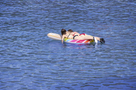 Two young girls swimming on air mattress in the seaの写真素材