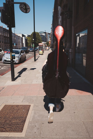 Vauxhall, London | UK - 2021.06.13: Young girl walking down the street carying Cello case on hot summer dayのeditorial素材