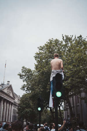 London | UK - 2021.07.12: Young English football fan sitting on the top of traffic light at Trafalgar Square without shirtのeditorial素材