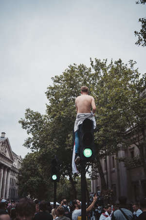 London | UK - 2021.07.12: Young English football fan sitting on the top of traffic light at Trafalgar Square without shirtのeditorial素材